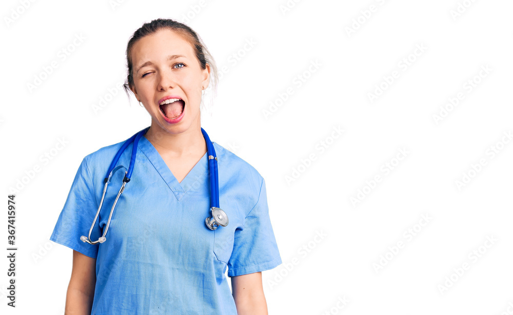 Young beautiful blonde woman wearing doctor uniform and stethoscope winking looking at the camera with sexy expression, cheerful and happy face. Young beautiful blonde woman wearing doctor uniform and stethoscope winking looking at the camera with sexy expression, cheerful and happy face.