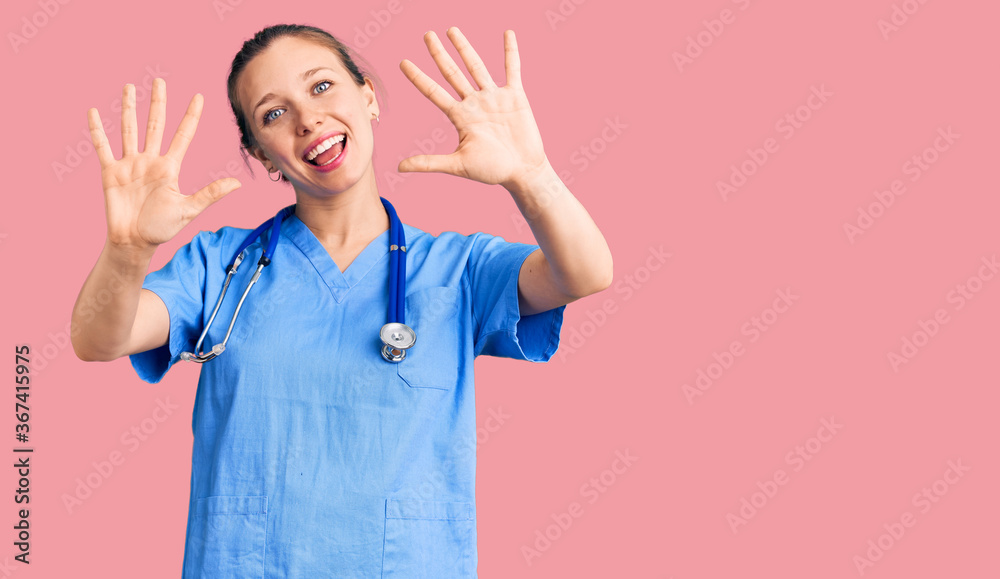 Obraz Young beautiful blonde woman wearing doctor uniform and stethoscope showing and pointing up with fingers number ten while smiling confident and happy.