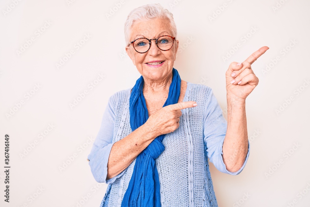 Senior beautiful woman with blue eyes and grey hair wearing casual sweater and scarf smiling and looking at the camera pointing with two hands and fingers to the side.