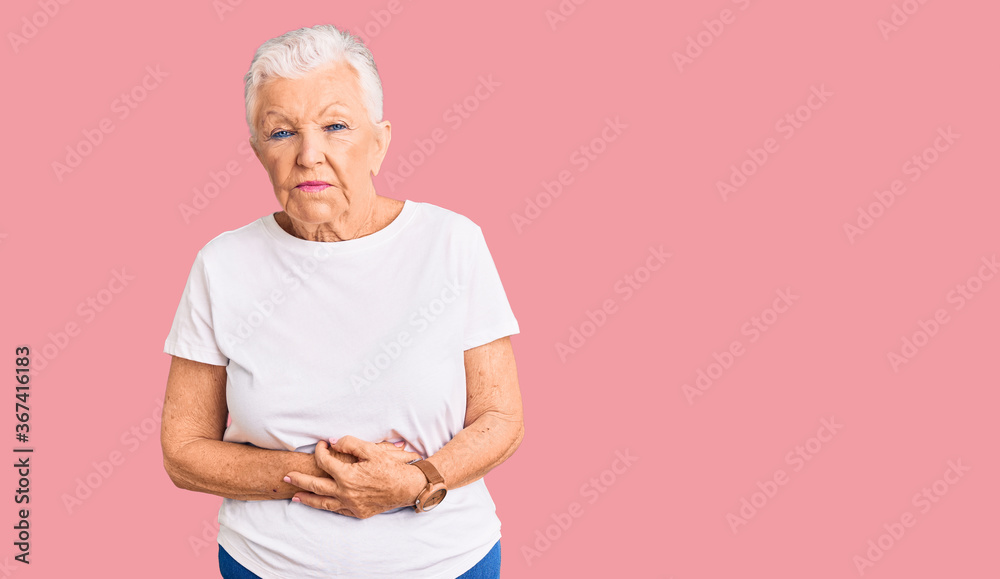 Senior beautiful woman with blue eyes and grey hair wearing casual white tshirt with hand on stomach because indigestion, painful illness feeling unwell. ache concept. Senior beautiful woman with blue eyes and grey hair wearing casual white tshirt with hand on stomach because indigestion, painful illness feeling unwell. ache concept.