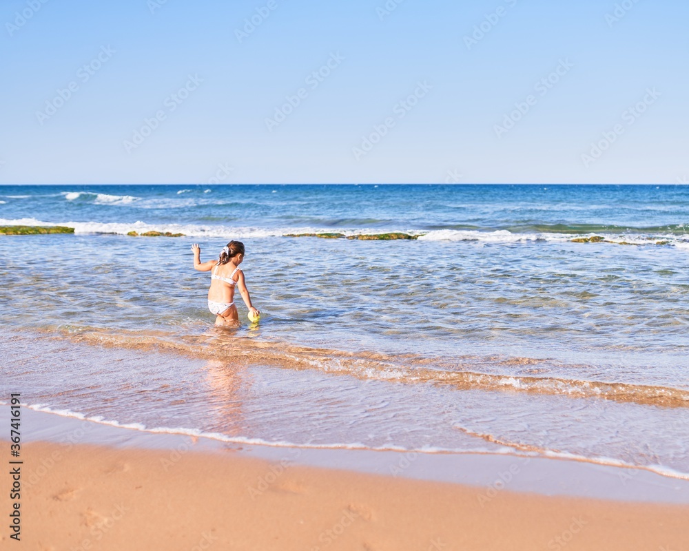 Adorable blonde child wearing bikini playing with water at the beach Adorable blonde child wearing bikini playing with water at the beach