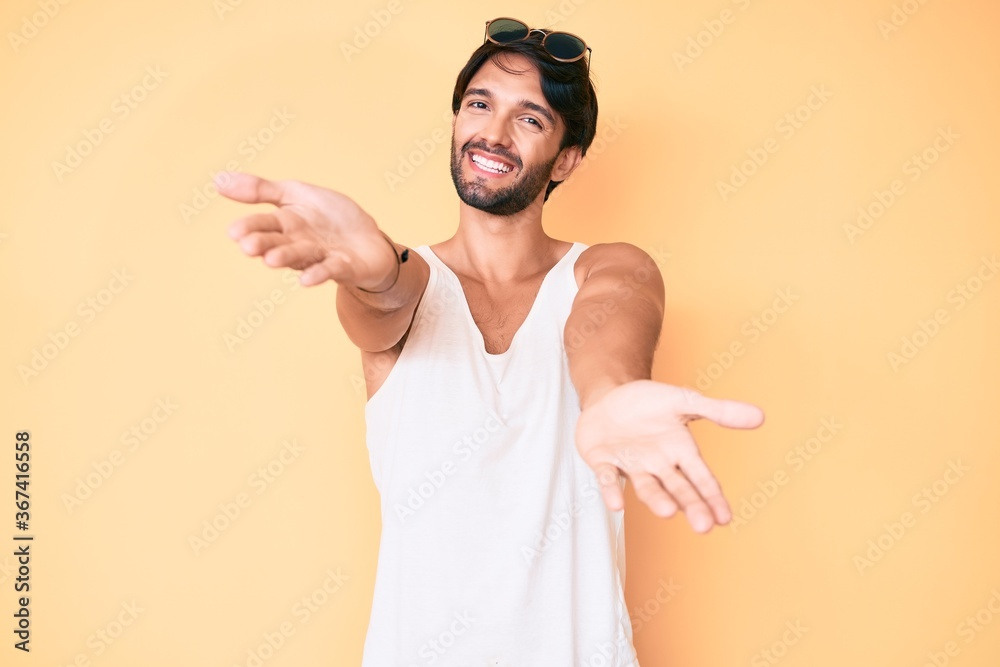 Handsome hispanic man wearing summer look and sunglasses looking at the camera smiling with open arms for hug. cheerful expression embracing happiness. Handsome hispanic man wearing summer look and sunglasses looking at the camera smiling with open arms for hug. cheerful expression embracing happiness.