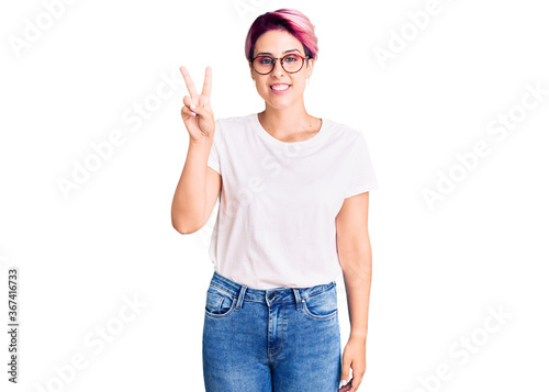 Young beautiful woman with pink hair wearing casual clothes and glasses showing and pointing up with fingers number two while smiling confident and happy.