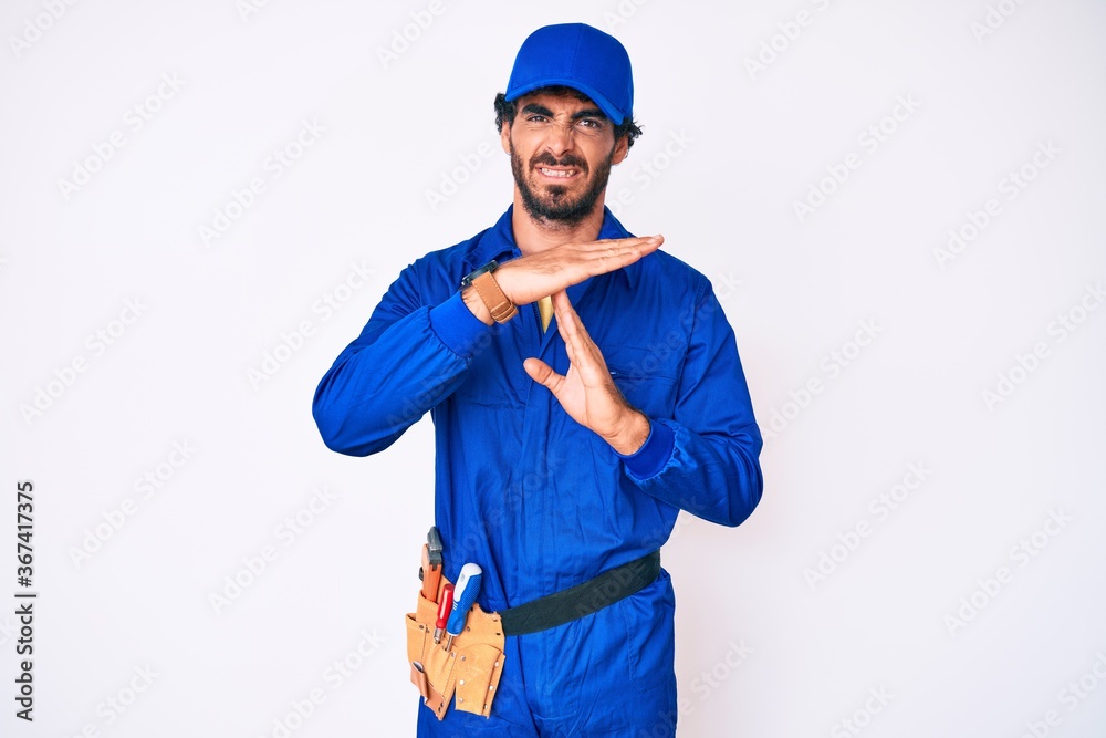 Handsome young man with curly hair and bear weaing handyman uniform doing time out gesture with hands, frustrated and serious face Handsome young man with curly hair and bear weaing handyman uniform doing time out gesture with hands, frustrated and serious face