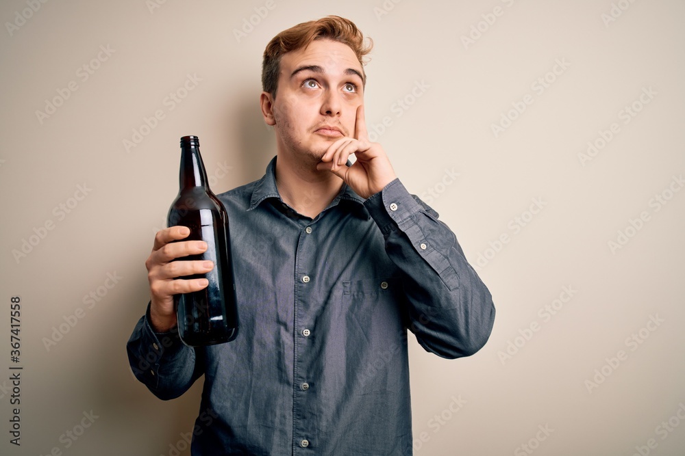 Young handsome redhead man drinking bottle of beer over isolated white background serious face thinking about question with hand on chin, thoughtful about confusing idea