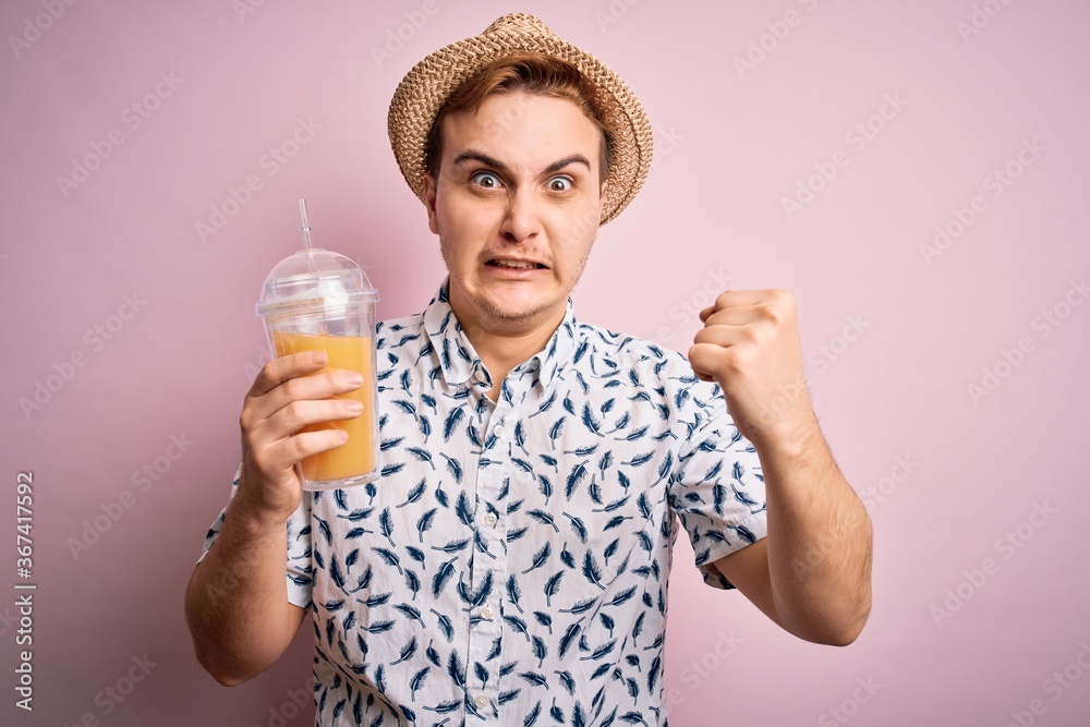 Young handsome redhead man on vacation drinking glass of healthy orange juice annoyed and frustrated shouting with anger, yelling crazy with anger and hand raised Young handsome redhead man on vacation drinking glass of healthy orange juice annoyed and frustrated shouting with anger, yelling crazy with anger and hand raised