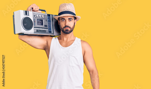Young hispanic man holding boombox, listening to music thinking attitude and sober expression looking self confident