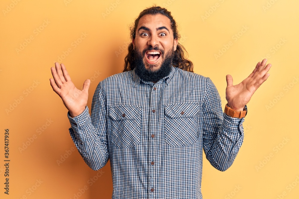 Naklejka premium Young arab man wearing casual clothes celebrating victory with happy smile and winner expression with raised hands