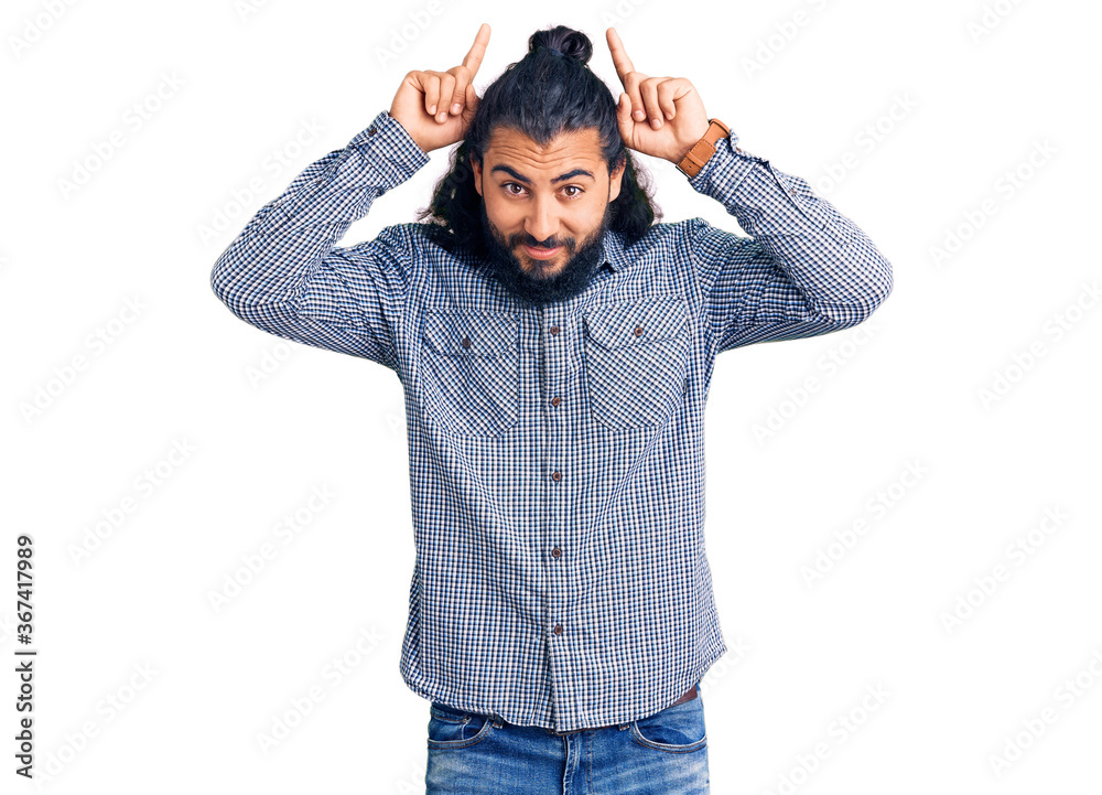 Young arab man wearing casual clothes doing funny gesture with finger over head as bull horns Young arab man wearing casual clothes doing funny gesture with finger over head as bull horns