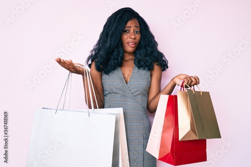 Young african american woman holding shopping bags clueless and confused expression. doubt concept.
