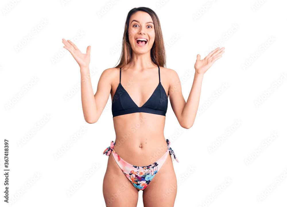 Young beautiful girl wearing bikini celebrating victory with happy smile and winner expression with raised hands