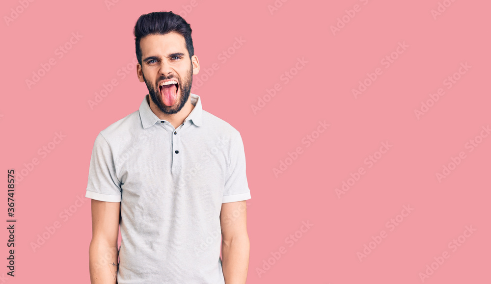 Fototapeta premium Young handsome man with beard wearing casual polo sticking tongue out happy with funny expression. emotion concept.