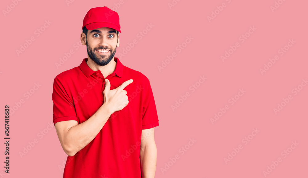Young handsome man with beard wearing delivery uniform cheerful with a smile on face pointing with hand and finger up to the side with happy and natural expression Young handsome man with beard wearing delivery uniform cheerful with a smile on face pointing with hand and finger up to the side with happy and natural expression