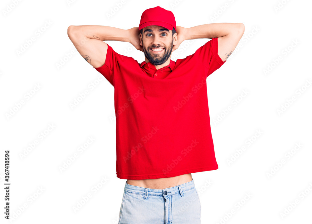 Fototapeta premium Young handsome man with beard wearing delivery uniform relaxing and stretching, arms and hands behind head and neck smiling happy