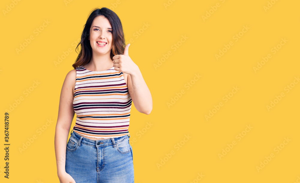 Beautiful young brunette woman wearing casual clothes smiling happy and positive, thumb up doing excellent and approval sign Beautiful young brunette woman wearing casual clothes smiling happy and positive, thumb up doing excellent and approval sign