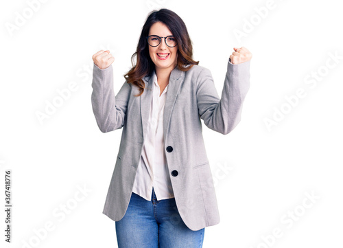 Beautiful young brunette woman wearing business clothes and glasses screaming proud, celebrating victory and success very excited with raised arms