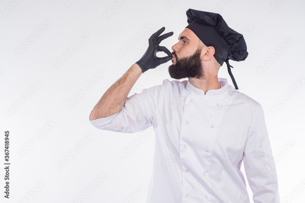 The chef approves. The bearded chef makes a sign with his hands very tasty. Excellent cuisine. A chef in a black hat and gloves. Man on a white background with a space for text. The chef approves. The bearded chef makes a sign with his hands very tasty. Excellent cuisine. A chef in a black hat and gloves. Man on a white background with a space for text.