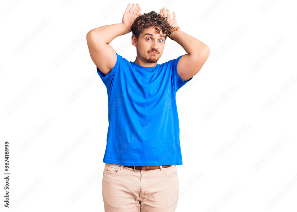 Young handsome man with curly hair wearing casual clothes doing bunny ears gesture with hands palms looking cynical and skeptical. easter rabbit concept. Young handsome man with curly hair wearing casual clothes doing bunny ears gesture with hands palms looking cynical and skeptical. easter rabbit concept.