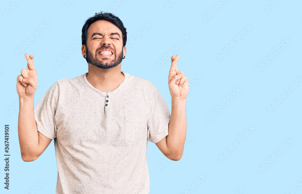 Fototapeta premium Young hispanic man wearing casual clothes gesturing finger crossed smiling with hope and eyes closed. luck and superstitious concept.