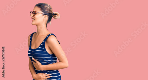 Young beautiful woman wearing casual clothes and glasses with hand on stomach because nausea, painful disease feeling unwell. ache concept. photo
