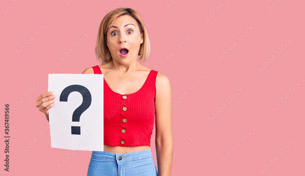 Young blonde woman holding question mark scared and amazed with open mouth for surprise, disbelief face Young blonde woman holding question mark scared and amazed with open mouth for surprise, disbelief face