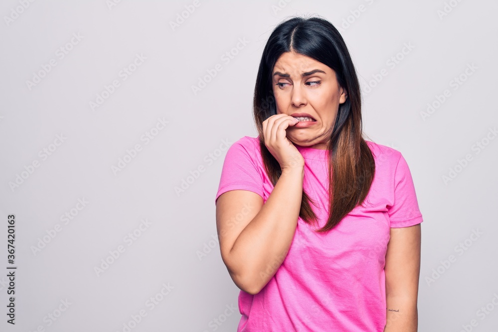 Young beautiful brunette woman wearing casual pink t-shirt standing over white background looking stressed and nervous with hands on mouth biting nails. Anxiety problem. Young beautiful brunette woman wearing casual pink t-shirt standing over white background looking stressed and nervous with hands on mouth biting nails. Anxiety problem.