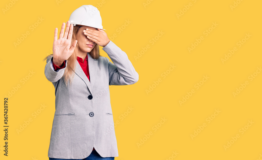 Beautiful young woman wearing architect hardhat covering eyes with hands and doing stop gesture with sad and fear expression. embarrassed and negative concept. Beautiful young woman wearing architect hardhat covering eyes with hands and doing stop gesture with sad and fear expression. embarrassed and negative concept.