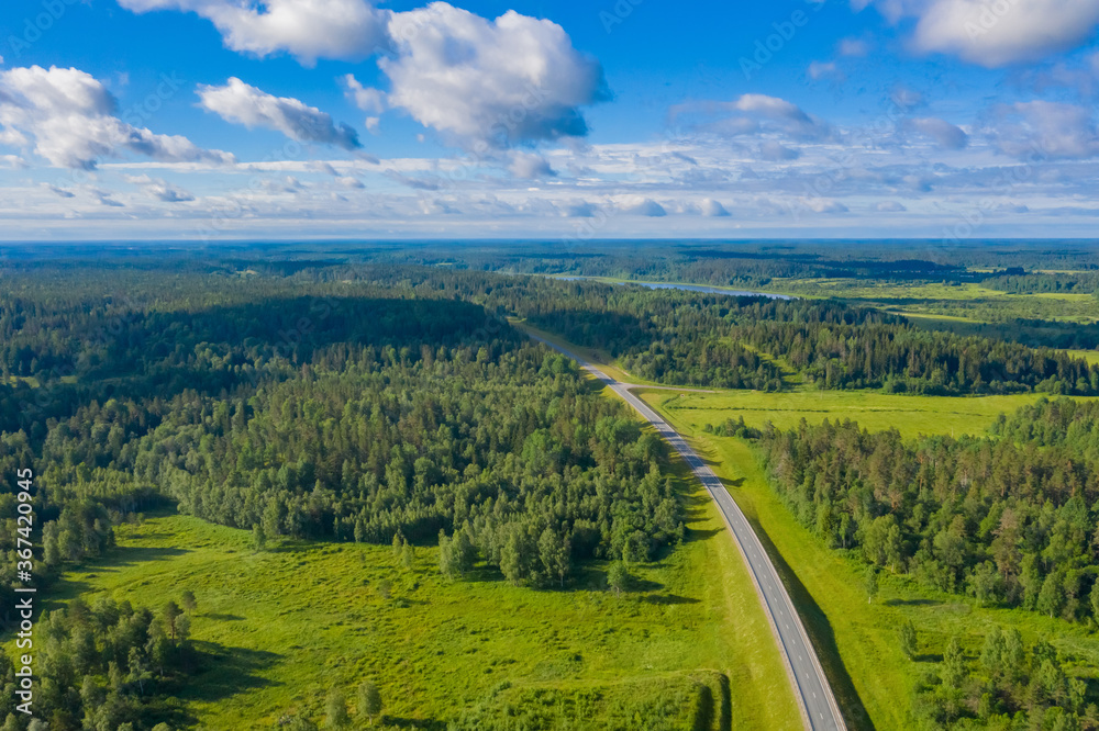 Highway and forests aerial photography. The road passes through the forest. Highway and beautiful natural landscape around. The forest and the road under the blue sky. Travel by car.