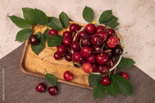 Red ripe cherries with leaves and twigs lying on wooden board.