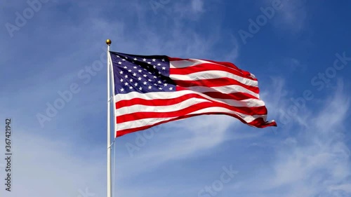 American flag waving in slow motion, with vibrant red white and blue colors lit by the sun, against blue sky for with copy space.