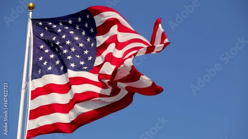 Bright American flag waving in the wind, in slow motion, with vibrant red white and blue colors lit by the sun, against blue sky for with copy space.