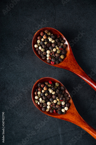 Mix of red and black pepper in wooden spoon on black background. Aromatic spice for cooking.