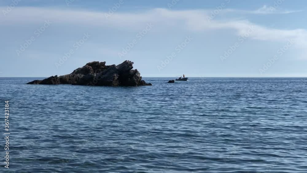 Boat and rock silhouette in blue calm sea Boat and rock silhouette in blue calm sea