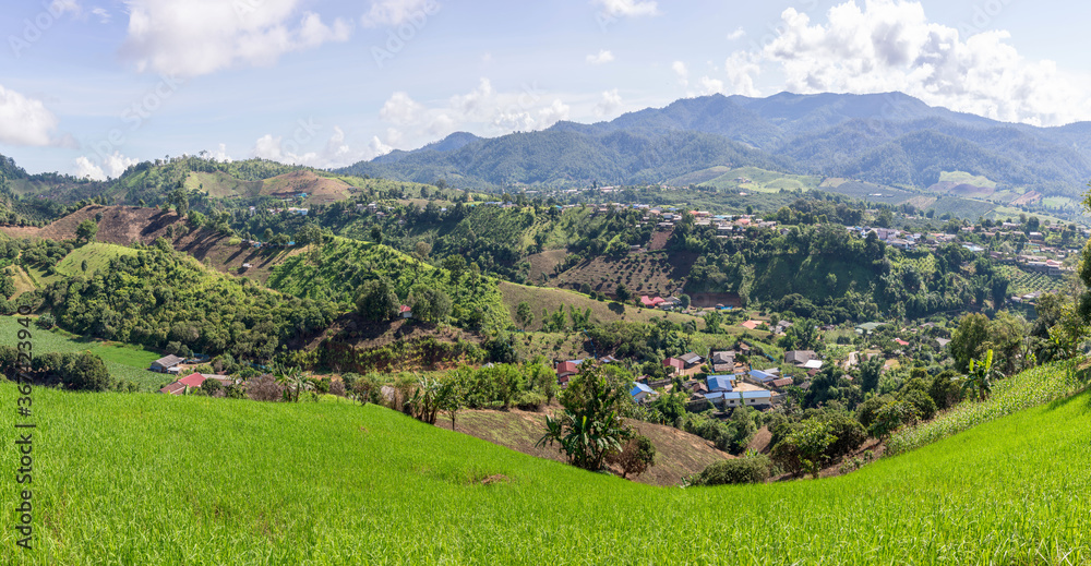 Panoramic of rice paddies farm with village surrounded by mountains. Thailand
