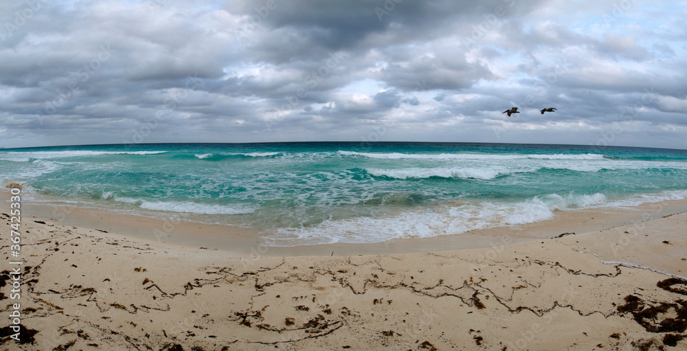 Vacations. Panorama view of the beach under a dramatic sky. The white sand, shore, coastline, turquoise color water ocean and sea waves in Cancun, Mexico.