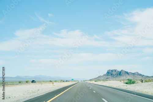 landscape of straight road running along barren land on both side. view of freeway stretches all the way to horizon on a sunny day.