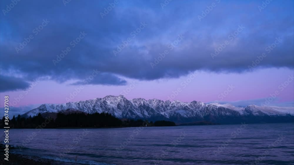 Time lapse: thick opaque stratus clouds blanket Lake Wakatipu with scenic view of jagged Remarkables mountain range in background at sunset, New Zealand, low vantage static, day to night Time lapse: thick opaque stratus clouds blanket Lake Wakatipu with scenic view of jagged Remarkables mountain range in background at sunset, New Zealand, low vantage static, day to night