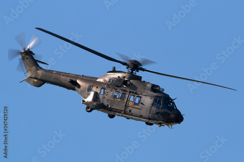 Camouflaged military helicopter flying against a blue sky.