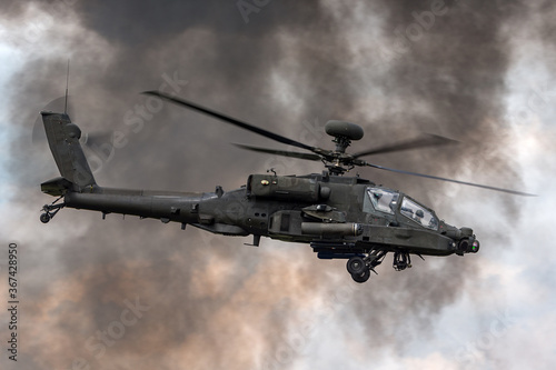 Army attack helicopter flying past dark smoke plumes.