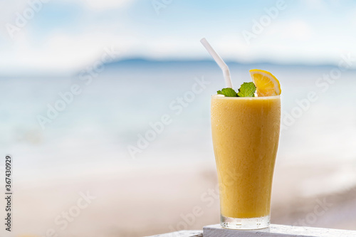 Fresh mango smoothie in glass on wood with outdoor background