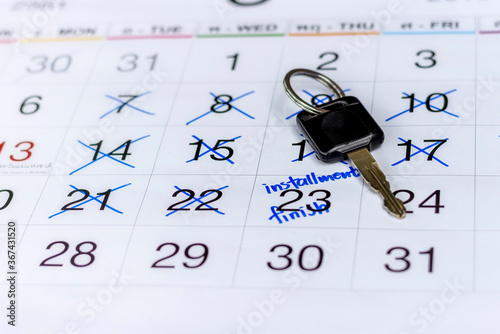 Closed up picture of car key on the white calendar with made marked on a date to mark appointment reminder of installment payments for car finance.