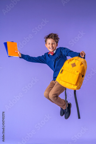 Foto cheerful schoolboy in uniform with backpack and books jumps on purple background