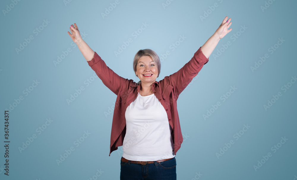 Senior blonde woman posing with hands up and smile toothily on a blue studio wall Senior blonde woman posing with hands up and smile toothily on a blue studio wall