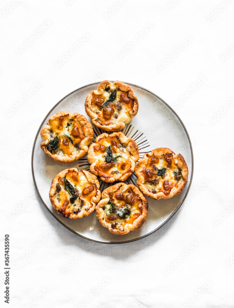 Minced meat, spinach, mozzarella cheese mini hand pies for appetizers, tapas, snack on a light background, top view Minced meat, spinach, mozzarella cheese mini hand pies for appetizers, tapas, snack on a light background, top view