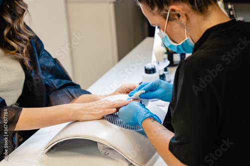 Aesthetician doing the manicure  filing the nails with a file to his client in a beauty center