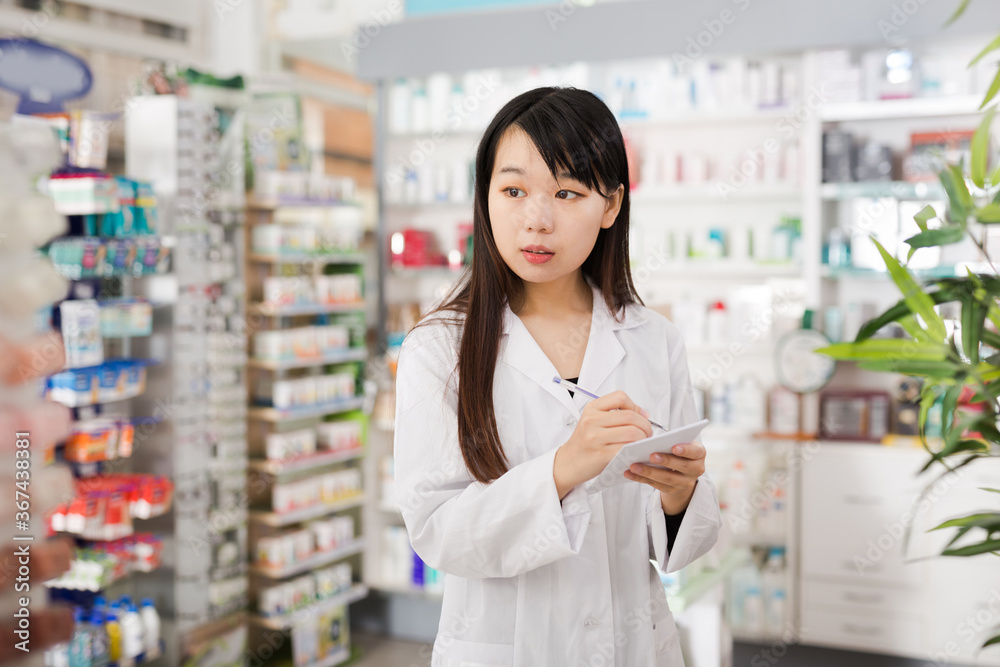 Chinese woman pharmacist keeps track of drugs in interior of pharmacy. High quality photo