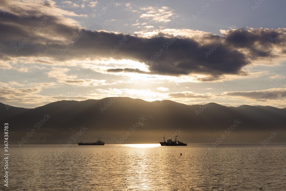 ships at sea against the background of the rays of dawn breaking through the mountains