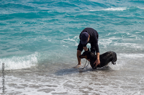 ANTALYA,KONYAALTI-TURKEY - APRIL18, 2019:Adult a man playing his dog doberman pinscher at beach. photo