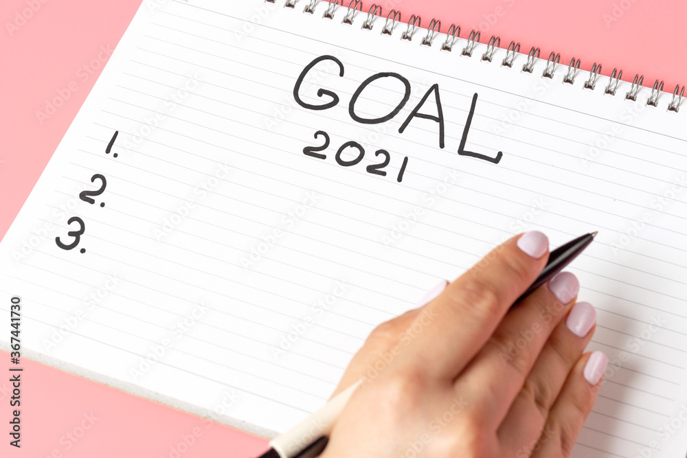 Girl writes in notepad of goal for 2021 on a pink background Girl writes in notepad of goal for 2021 on a pink background