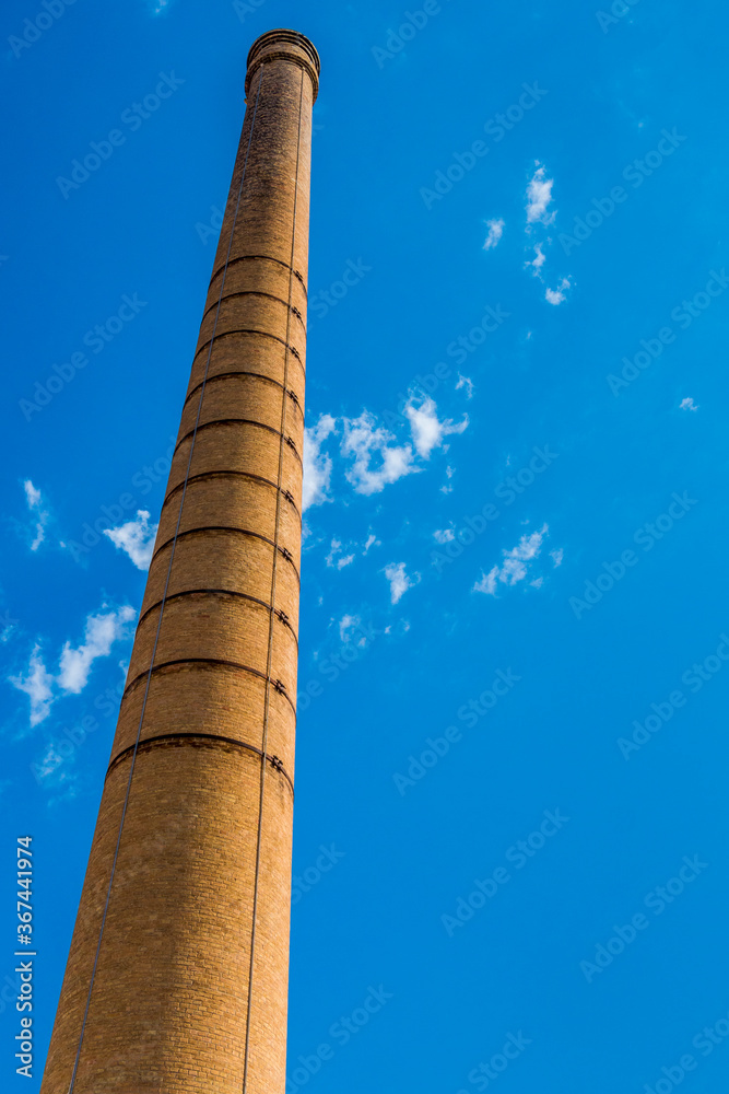 Tall and old brick chimney against a cloudy blue sky